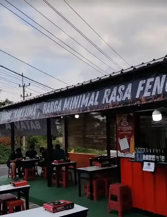 Meja dengan kompor grill, bangku merah, dan spanduk Batavia